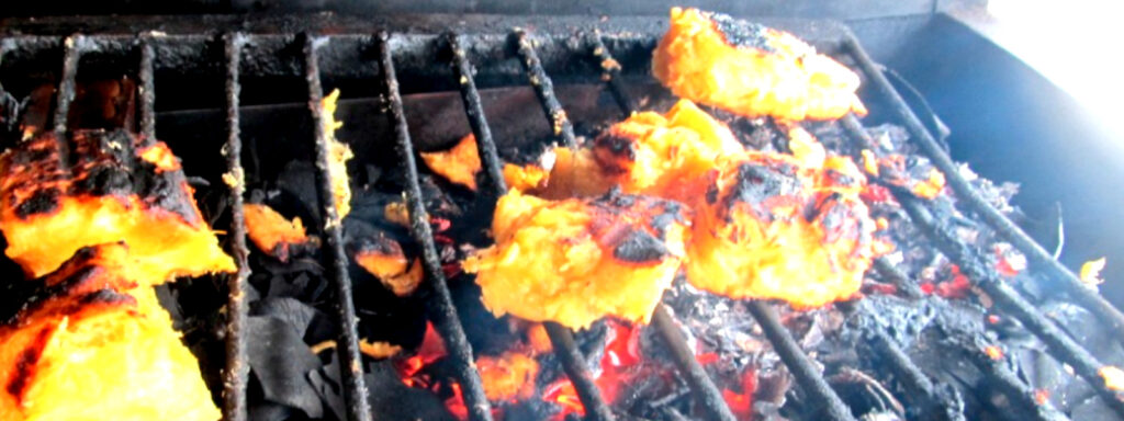 A imagem mostra uma grelha de ferro com alguns pedaços de mandioca no churrasco.